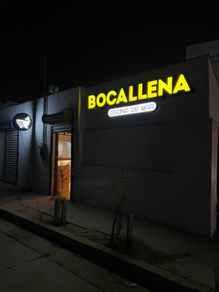 Letrero Bocallena amarillo y Cocina de Mar blanco de noche, mascota marina en círculo