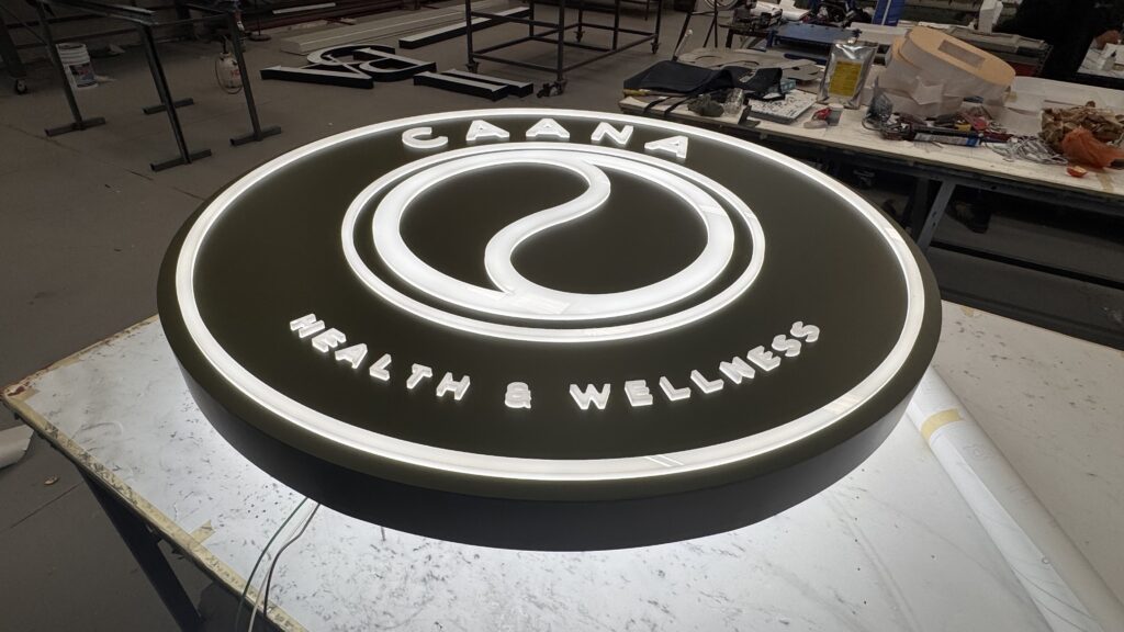 Letrero ovalado Caana Health Wellness verde oscuro con logo circular blanco