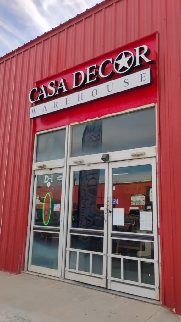 Fachada Casa Decor Warehouse roja con letrero blanco y open verde puerta