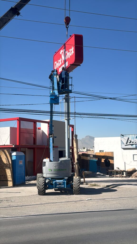 Grúa elevadora instalando letrero rojo Chick N Chick Drive Thru en poste