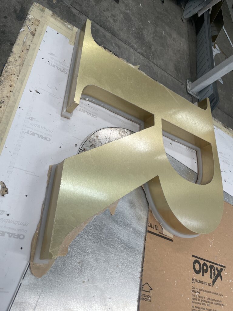 Detalle de letras doradas Crown Dollar en proceso de montaje con aislante protector