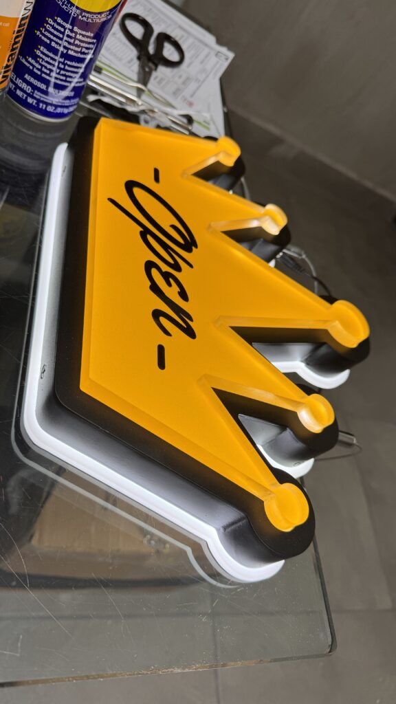Letrero Open en forma de corona amarillo y negro con LED en bordes