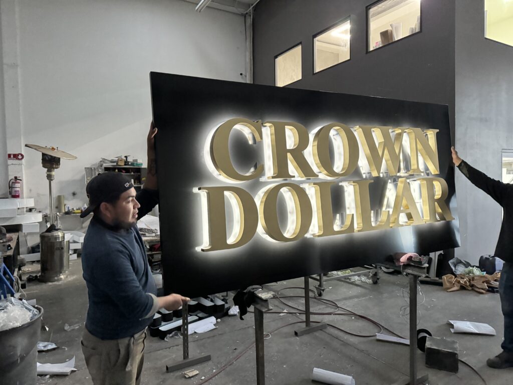 Letrero Crown Dollar con letras doradas retroiluminadas sobre fondo negro en taller