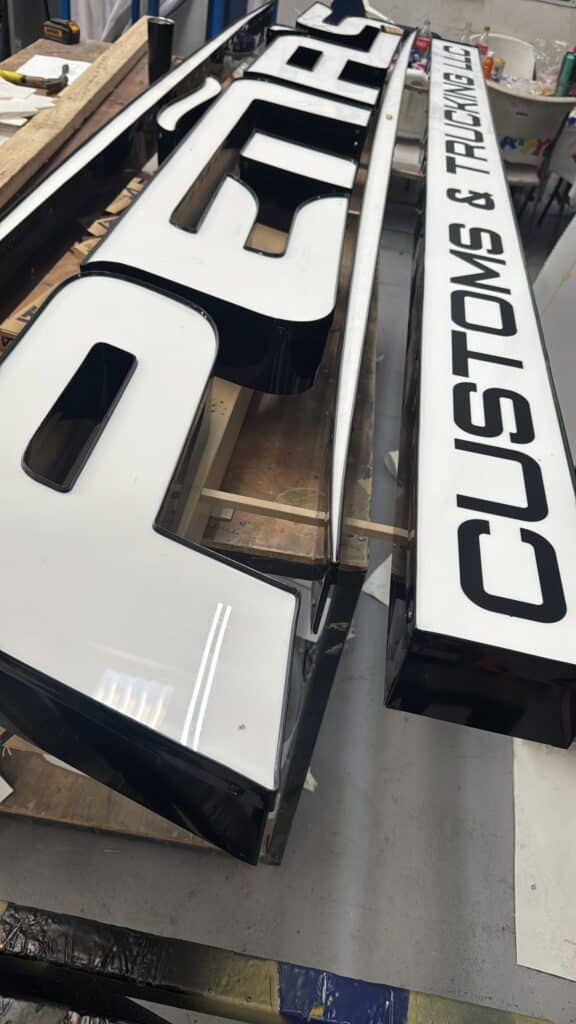 Letrero blanco y negro Customs & Trucking LLC en fase de fabricación en taller