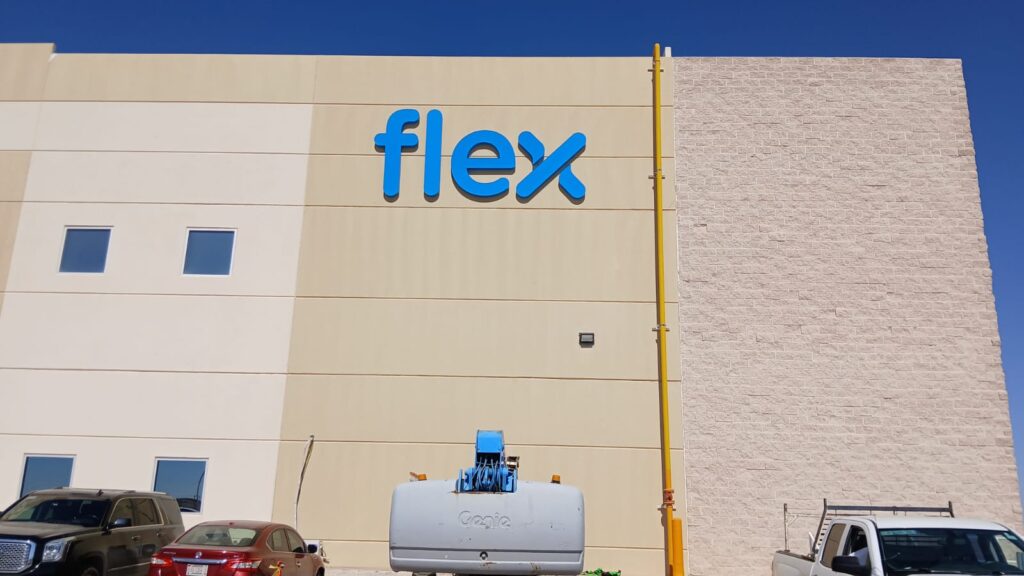 Letras flex azul minúsculas instaladas sobre fachada beige de nave industrial