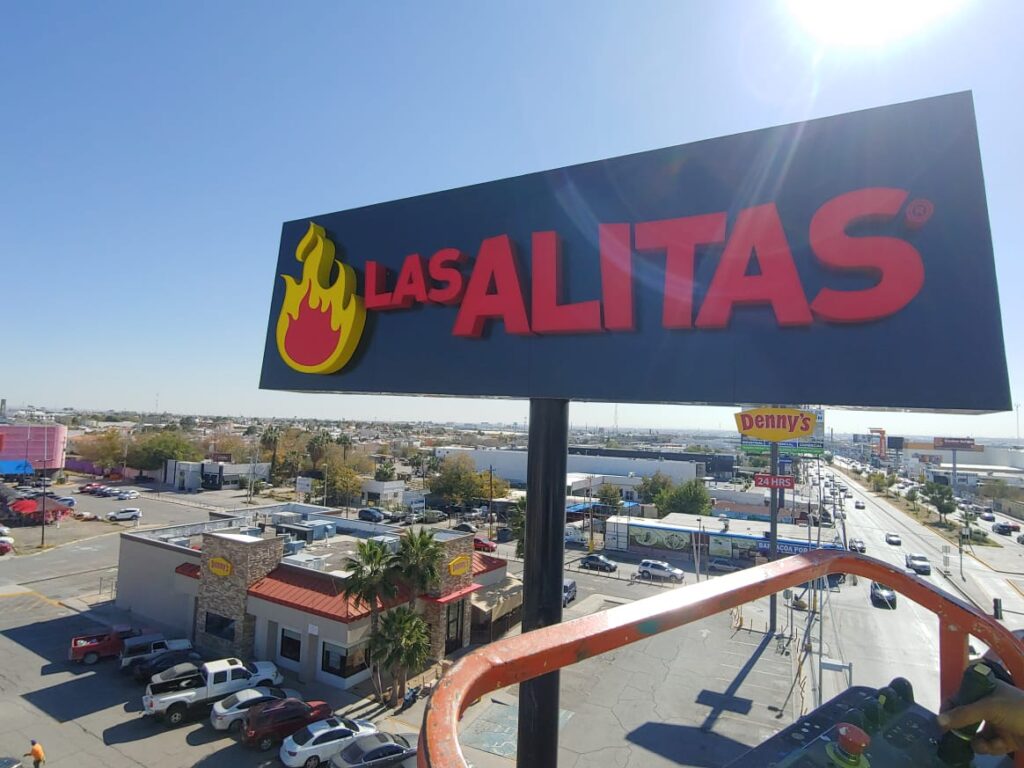 Espectacular elevado Las Alitas con letrero rojo y flama amarilla contra cielo azul