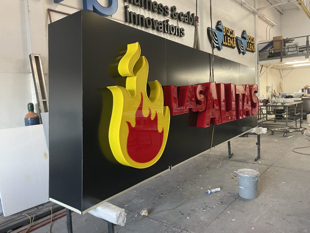 Letrero Las Alitas en proceso de fabricación con flama roja y amarilla en taller