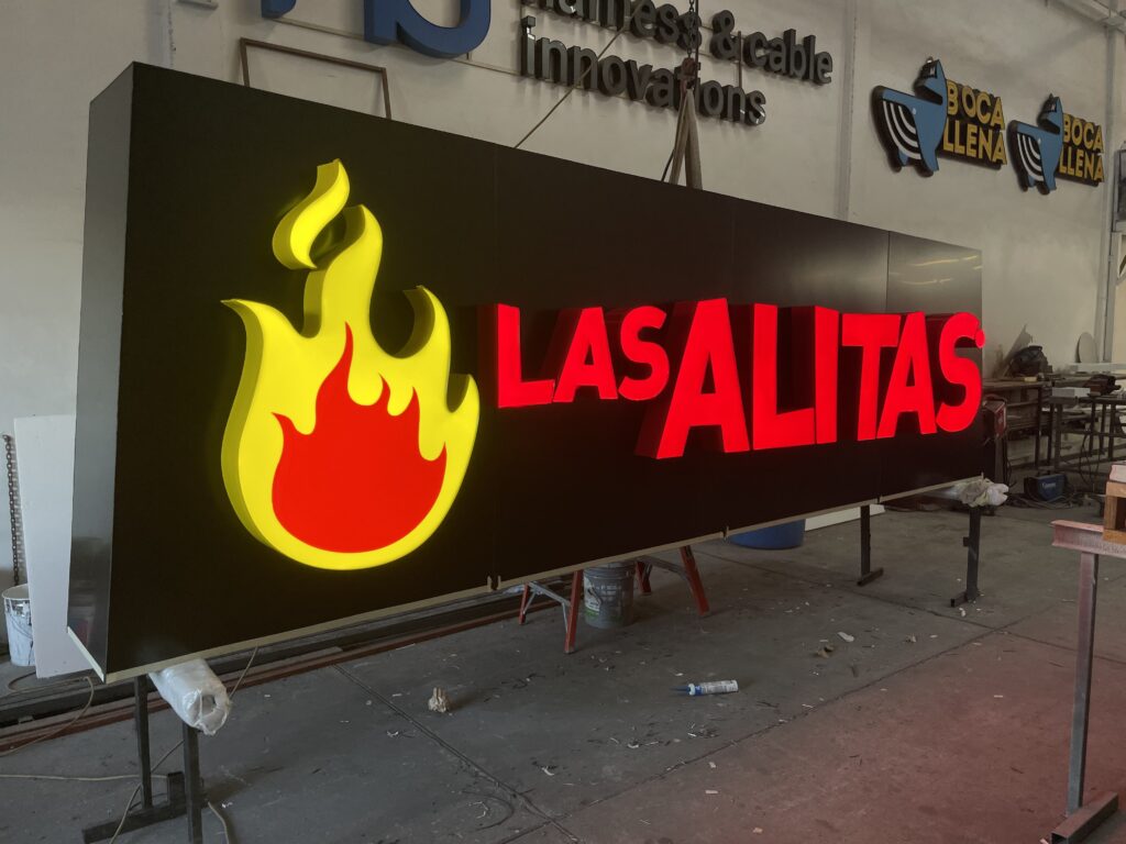 Logo flama amarillo y rojo de Las Alitas instalado en fachada de azulejos de piedra