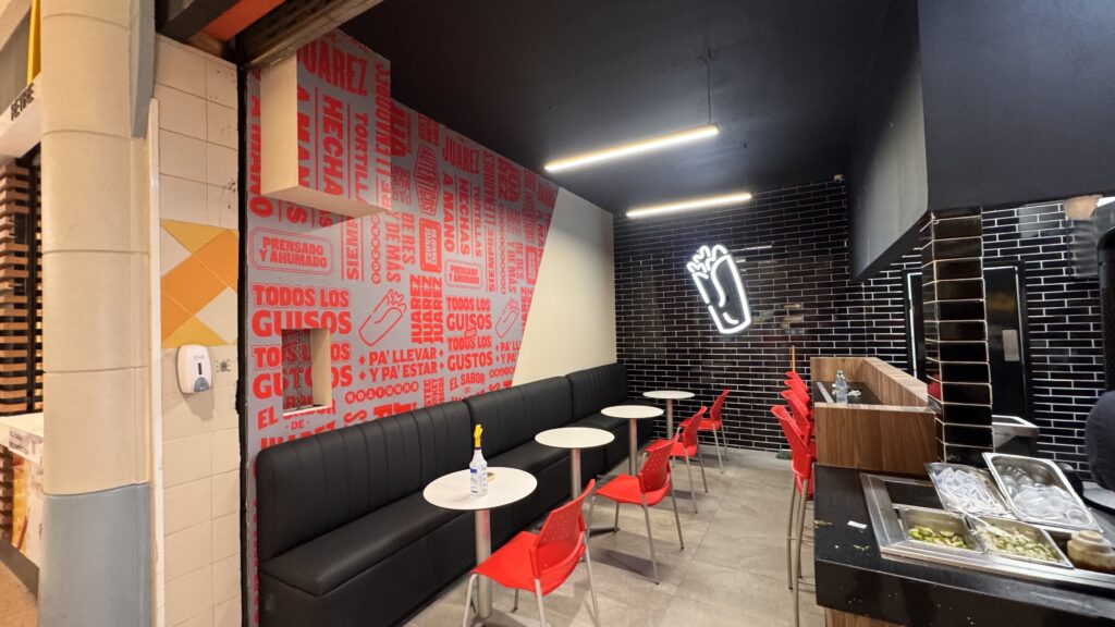 Interior restaurante con panel rojo, sillas rojas, neón blanco en pared