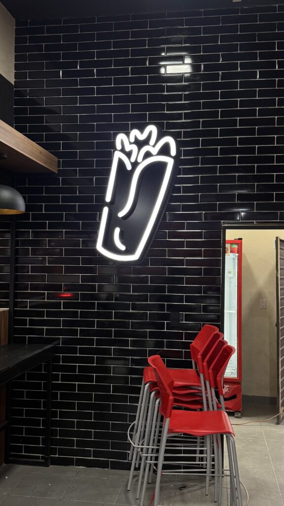 Neón blanco forma de burrito en pared negra ladrillo con sillas rojas