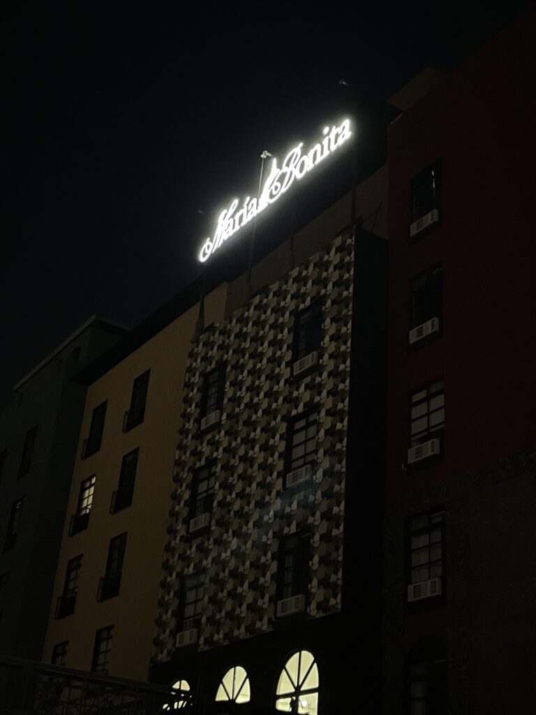 Letrero María Bonita en script blanco iluminado de noche en fachada