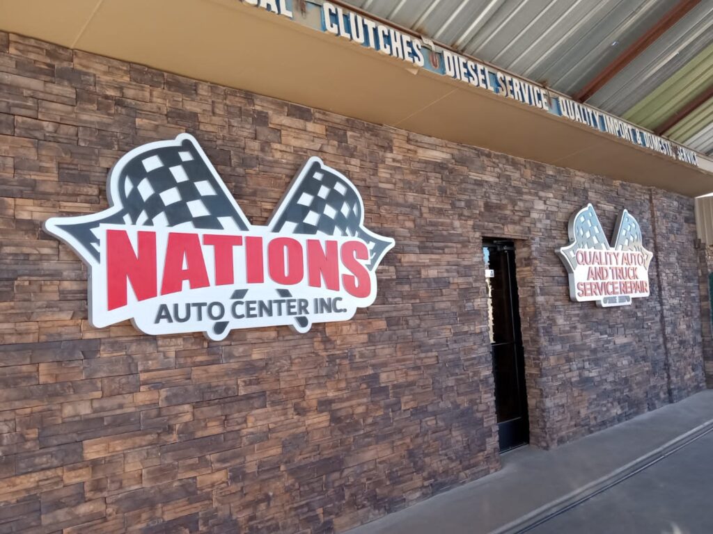Letrero principal Nations Auto Center con banderas en rojo instalado en fachada de piedra