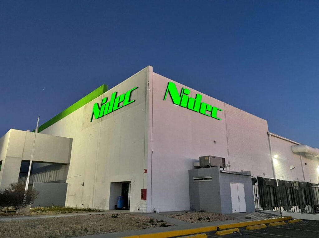 Logo Nidec verde neon retroiluminado en esquina edificio blanco noche