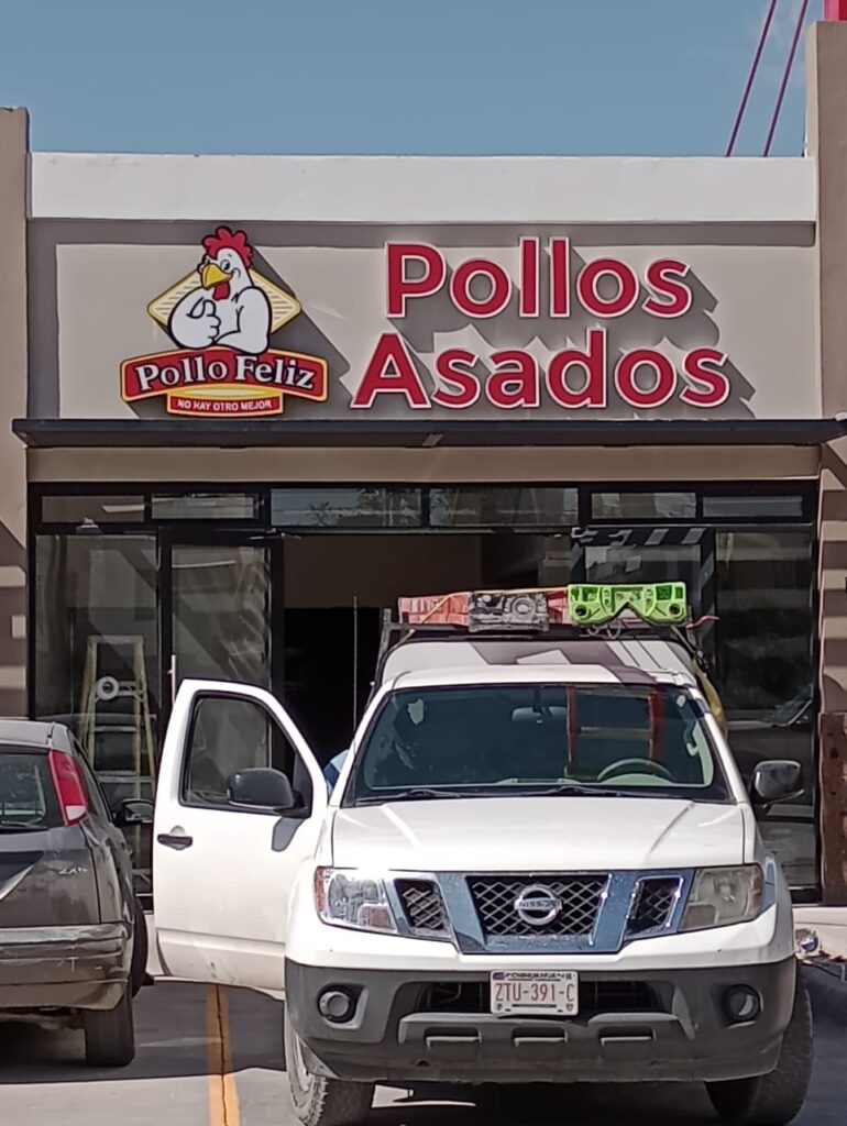 Letrero Pollo Feliz logo pollo texto rojo Pollos Asados en fachada día