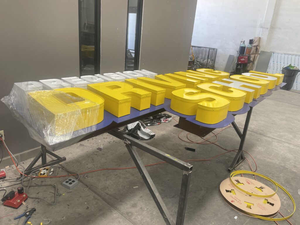 Letras Precision blanco y Driving School amarillo en fabricación taller