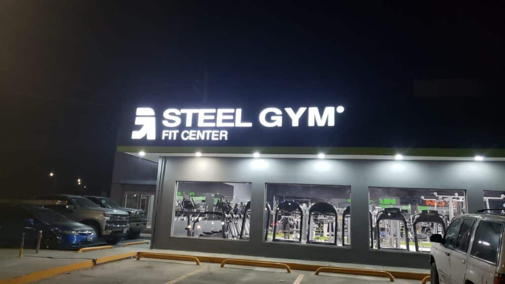 Letrero Steel Gym Fit Center blanco retroiluminado noche sobre fachada