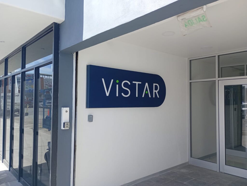 Cartel Vistar azul marino en fachada exterior blanca de día con entrada visible